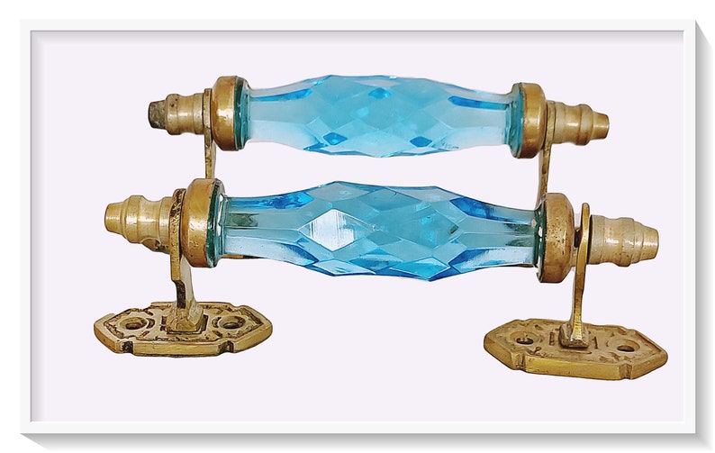May include: Two antique glass door handles with brass fixtures. The handles are faceted and have a light blue color.