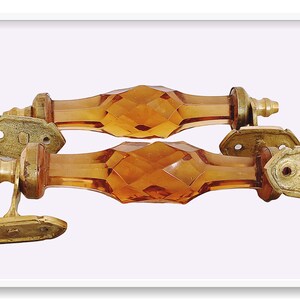 May include: Two amber glass cabinet door pulls with brass accents. The pulls are faceted and have a diamond-like pattern.