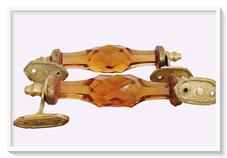 May include: Two amber glass cabinet door pulls with brass accents. The pulls are faceted and have a diamond-like pattern.