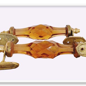 May include: Two amber glass cabinet door pulls with brass accents. The pulls are faceted and have a diamond pattern.