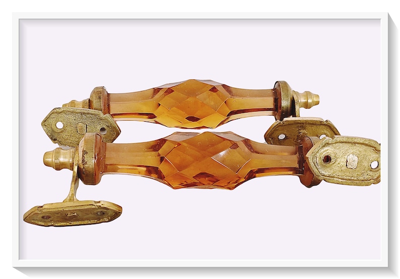 May include: Two amber glass cabinet door pulls with brass accents. The pulls are faceted and have a diamond pattern.