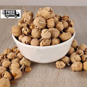 Peut inclure: Un bol en céramique blanc rempli de graines séchées de couleur beige. Quelques graines débordent du bol sur la surface. Les graines ont une forme ronde et texturée.