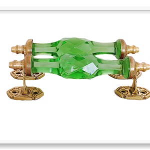 May include: A pair of green glass door handles with brass accents. The handles are faceted and have a diamond-like pattern. The brass accents are ornate and have a decorative design.