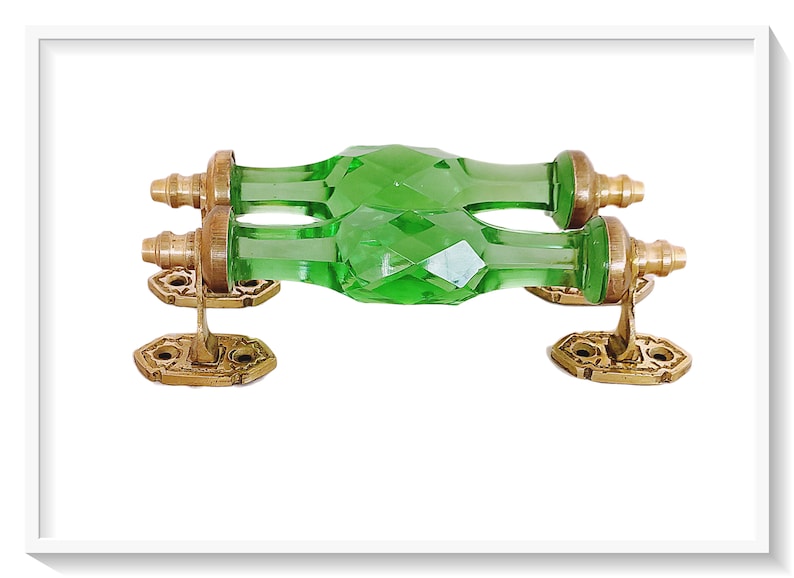 May include: A pair of green glass door handles with brass accents. The handles are faceted and have a diamond-like pattern. The brass accents are ornate and have a decorative design.