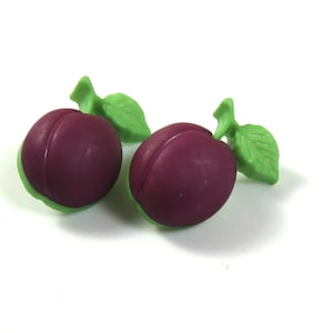 May include: Two purple plastic plums with green plastic leaves. The plums are about the size of a quarter.