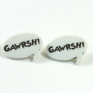 May include: A pair of white speech bubble earrings with the word "GAWRSH!" printed in black.