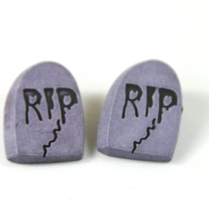 May include: Two small, gray, tombstone-shaped earrings with the word "RIP" written in black on each.