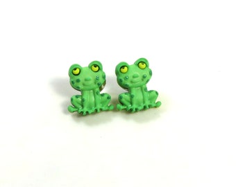 May include: A pair of green frog stud earrings with yellow eyes. The frogs are sitting with their legs crossed.