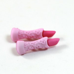 Puede incluir: Dos pintalabios de juguete de plástico rosa con un diseño floral. Los pintalabios están cerrados y tienen una tapa rosa.