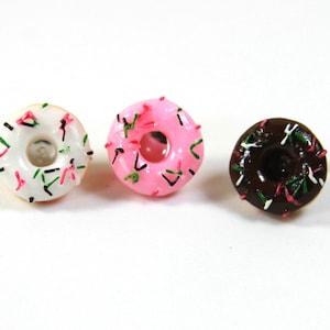 Puede incluir: Tres mini donuts con chispas de colores. Los donuts son blancos, rosados y marrones.