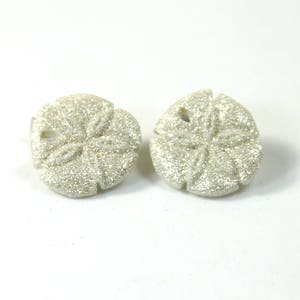 Puede incluir: Un par de pendientes de plata con forma de dólar de arena con un acabado brillante.