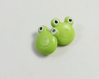 May include: Two green frog-shaped buttons with black eyes and a smiling mouth.
