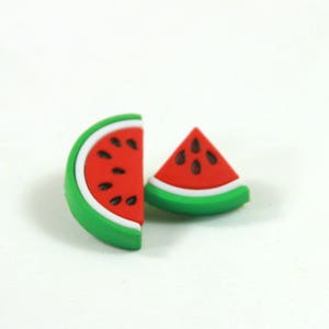 Op de afbeelding: Twee watermeloen-vormige oorbellen, een is een volledige plak en de andere is een wig. Beide zijn rood met zwarte zaden en groene schillen.