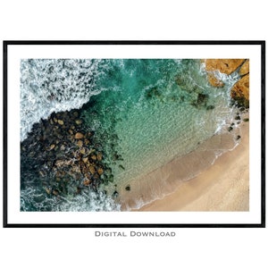 May include: An aerial view of a rocky coastline with turquoise water and white sand. The waves are crashing against the rocks, creating a beautiful contrast of colors.