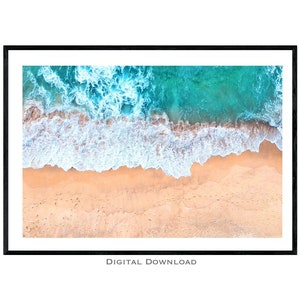 May include: An aerial view of a sandy beach with turquoise water and white foamy waves crashing on the shore.