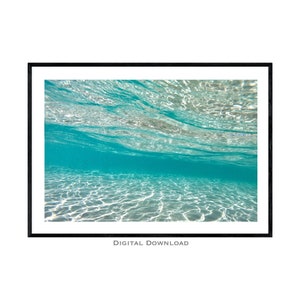 May include: An underwater photograph of a turquoise blue ocean with white light reflecting off the sandy bottom.