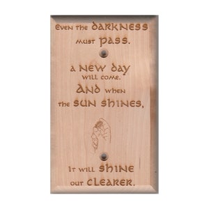 Puede incluir: Una cubierta de interruptor de luz de madera clara con la cita "Incluso la oscuridad debe pasar. Un nuevo día vendrá. Y cuando el sol brille, brillará más fuerte." La cita está tallada en la madera y hay una pequeña imagen de una mano sosteniendo una flor.