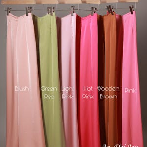 May include: A collection of long, flowing skirts in various colors, including blush, green pea, light pink, hot pink, wooden brown, and pink, hanging on a wooden rack. The skirts have a smooth, silky texture. The text "Ao Dai Joy" is visible.