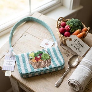 May include: A rectangular beaded handbag featuring a light blue and white striped pattern with a central embroidered basket of vegetables. The bag has a light blue strap and two attached tags, one reading Handcrafted in India.