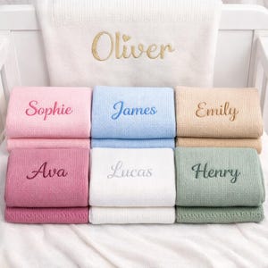 May include: A collection of personalized baby blankets in various pastel colors, including pink, blue, and green. Each blanket is embroidered with a name in a complementary color, such as "Oliver," "Sophie," and "James."