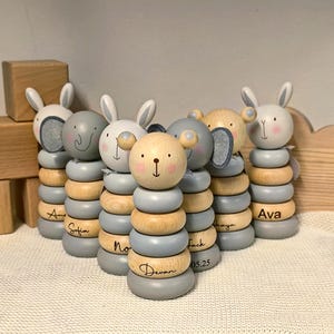 May include: A collection of wooden stacking toys, each topped with an animal head. The toys feature a stack of wooden and grey rings. Names are engraved on the base rings. A delightful and educational toy for young children.