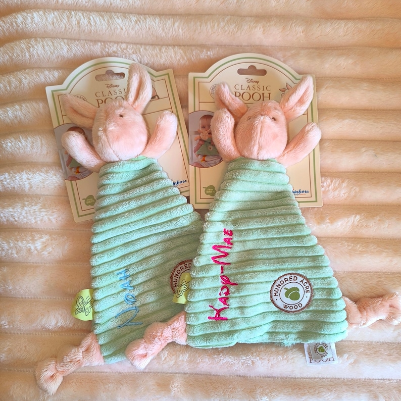 May include: Two plush baby toys featuring a pink bunny head and a light green, corduroy body. The toys have the words "Kasp-Mae" and "Noah" embroidered on the body. Each toy has a tag that reads "Disney Classic Pooh".