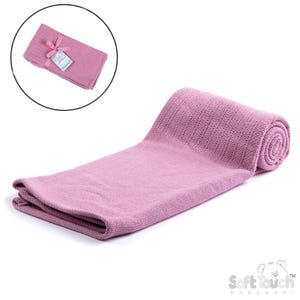 May include: A soft, pink baby blanket, partially rolled and partially folded. The blanket is made of a knitted material. A smaller, folded blanket with a tag and ribbon is in a circular inset.