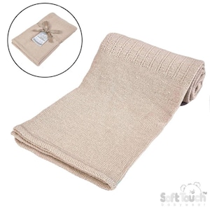 May include: A beige knitted baby blanket, partially rolled, with a folded section at the bottom. A smaller, folded blanket with a tag and ribbon is in a circular inset. The blanket is made of a soft, breathable material.