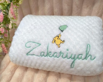 Könnte beinhalten: Weiße Babydecke aus Plüsch mit dem Namen "Zakariyah" in hellgrüner Schrift gestickt. Ein gelber Cartoon-Bär, der einen grünen Ballon hält, ist über dem Namen gestickt. Die Decke hat eine strukturierte Oberfläche.