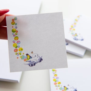 Könnte beinhalten: Ein Stapel weißer Notizblöcke mit einem farbenfrohen Design eines Flugzeugs, das durch eine Spur von Blasen fliegt. Das Flugzeug hat ein Comic-Gesicht und ein kleiner Vogel fliegt daneben.