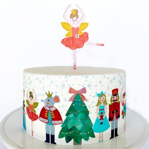 May include: A white cake decorated with a Nutcracker theme. The cake is decorated with a ballerina, a mouse king, a Christmas tree, and a nutcracker soldier. The cake is topped with a ballerina figurine.