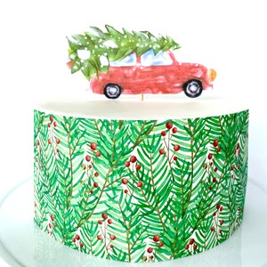 May include: A red car carrying a green Christmas tree on top, with a white snowy background. The car is on top of a round cake decorated with a green and white pattern of pine branches and red berries.