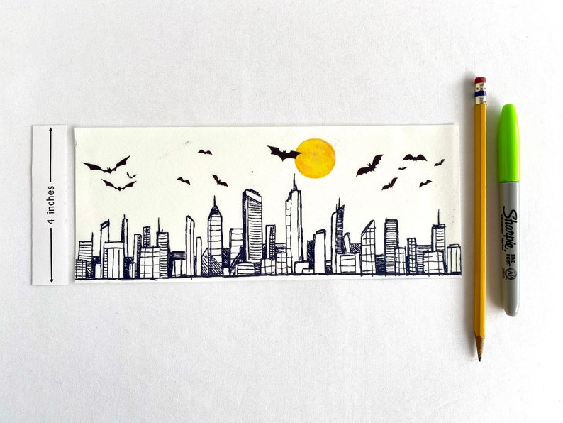 Puede incluir: Un dibujo a tinta en blanco y negro de un horizonte de ciudad con murci&eacute;lagos volando por encima y un sol amarillo. El dibujo est&aacute; sobre un fondo blanco y mide 10 cm de alto.