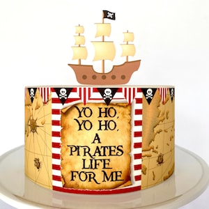 May include: A pirate-themed cake decorated with a brown ship with white sails and a black skull and crossbones flag. The cake is wrapped in a red and white striped paper with a pirate map and the text "Yo ho, yo ho, a pirates life for me".