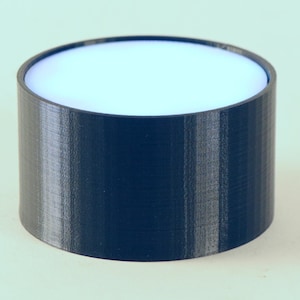 Op de afbeelding: Een cilindrisch object met een donkerblauwe buitenkant en een witte binnenkant. Het object is een eenvoudig, modern ontwerp, waarschijnlijk 3D-geprint, en heeft een glad, schoon uiterlijk. Het object heeft een diameter van ongeveer 7,6 cm en is 7,6 cm hoog.