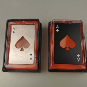 Può includere: Due apribottiglie in metallo a forma di carte da gioco. La carta a sinistra è argentata con un asso di picche nero e la carta a destra è nera con un asso di picche rosso.