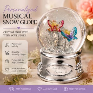 Peut inclure: Une boule à neige musicale avec deux papillons colorés sous un dôme en verre. La base argentée comporte une plaque gravée avec le texte 'You & Me Forever' et un cœur. Le texte 'Personalized MUSICAL SNOW GLOBE' est visible à côté.