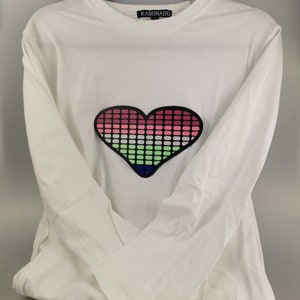May include: White long-sleeved t-shirt with a black heart-shaped graphic on the front. The heart is made up of small squares in shades of pink, green, blue, and white.