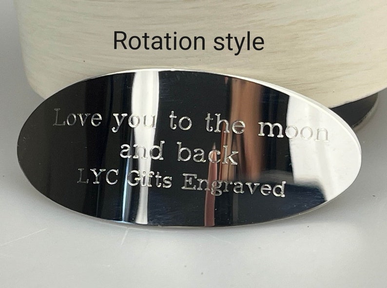 May include: A polished, oval-shaped metal plaque with engraved text. The text reads "Love you to the moon and back" and "LYC Gifts Engraved". The words "Rotation style" are above the plaque.