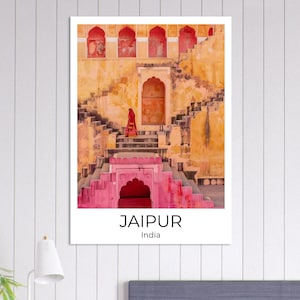 May include: A framed print featuring a stepwell in Jaipur, India. The image showcases a person in red attire descending the stairs of the ancient structure. The steps are painted in shades of yellow and pink, with the text "JAIPUR India" at the bottom.