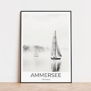 May include: A black and white photograph of two sailboats on a lake. The sailboats are in the distance, and the lake is surrounded by trees. The photo is framed in a black frame and has the text "AMMERSEE Germany" at the bottom.
