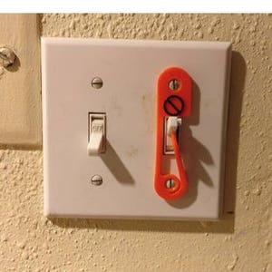 以下が含まれることがあります： 白い壁に、赤い安全カバーが付いた白いライトスイッチ。
