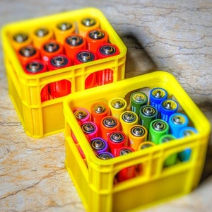 Puede incluir: Dos cajas de plástico amarillas llenas de pilas AA de colores. Las cajas tienen un patrón de cuadrícula y están apiladas una encima de la otra.