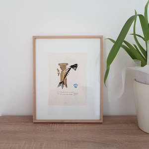 Può includere: Una stampa incorniciata di uno scheletro di pesce nero e giallo con una conchiglia blu. La stampa è su sfondo bianco con una citazione scritta a mano in francese.