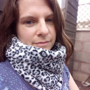 May include: A woman wearing a blue and white patterned shirt with a white and black leopard print scarf.