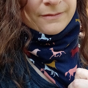 Puede incluir: Cuello de color azul marino con un estampado repetido de caballos en blanco, rosa, amarillo y rojo. El cuello está hecho de una tela suave y se lleva alrededor del cuello.