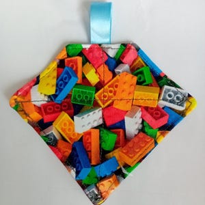 May include: A diamond-shaped pot holder with a colourful pattern of toy building blocks. The pot holder has a blue ribbon loop for hanging.