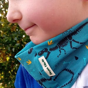 May include: A turquoise blue neck warmer with a dinosaur skeleton print and a white label that says "Devon Made".