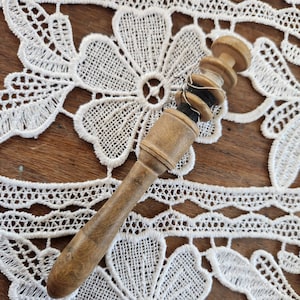 Op de afbeelding: Een houten spoel met een spoel zwart garen, liggend op een wit kantonderleg.