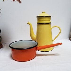 Può includere: Una caffettiera smaltata gialla con bordo nero e una pentola smaltata arancione abbinata con bordo nero.
